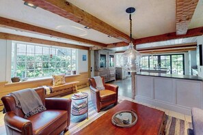 A spacious living area with a leather sofa, a coffee table, and a large window offering a view of the outdoors. - Luxury Gallery District home steps from beach with chef’s kitchen & gardens (Provincetown)