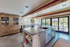 A kitchen with wooden cabinets, a central island, and large windows. - Luxury Gallery District home steps from beach with chef’s kitchen & gardens (Provincetown)
