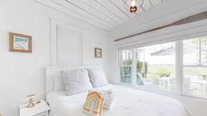 A bedroom with a large bed, a nightstand, a window with a view, and a ceiling light fixture. - Renovated Waterfront Retreat | Inspiring Views | Walk to Beach, Dining, Shops (Provincetown)