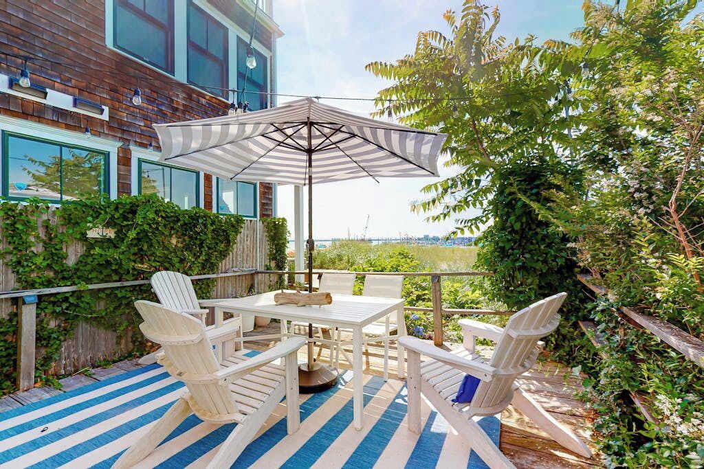 An outdoor patio with a table and chairs, an umbrella, and a view of a building and greenery.