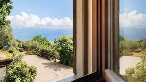 Blick aus einem Fenster auf einen Feldweg, Bäume und ein entferntes Gebirge.