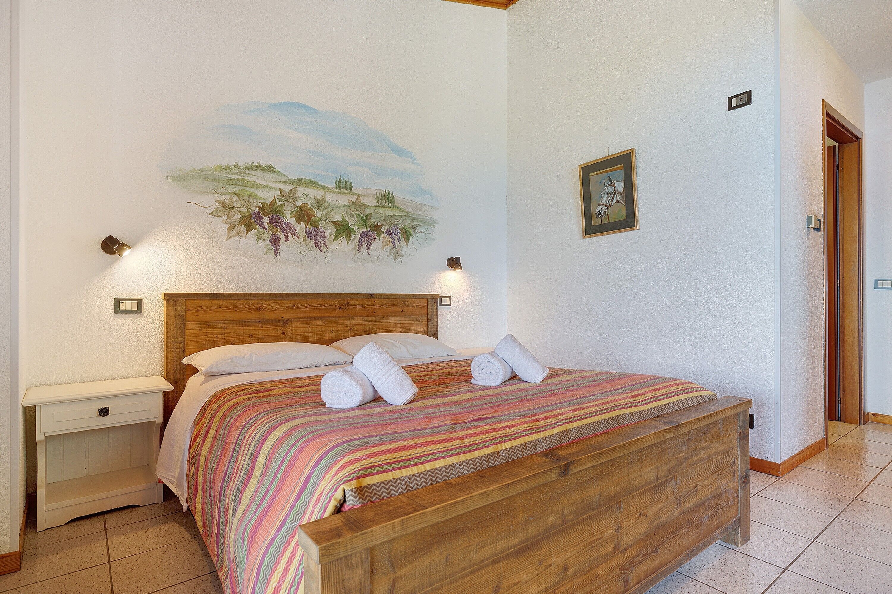 Un dormitorio con cama de madera, una mesita de noche, una lámpara de pared y un cuadro.