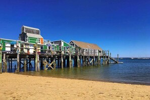 A pier with buildings extending over water, wooden stilts supporting the structure, and a clear blue sky. - Stunning West End Home | Historic Restoration | Dog-Friendly (Provincetown)