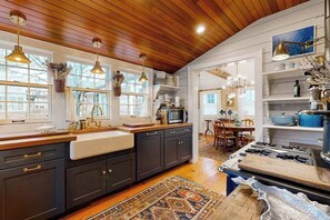 A kitchen with dark cabinets, a wooden countertop, a stove, and a dining area with a table and chairs. - Stunning West End Home | Historic Restoration | Dog-Friendly (Provincetown)