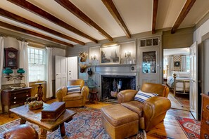 A traditional room with exposed wooden beams, a fireplace, leather furniture, and a patterned rug. - Stunning West End Home | Historic Restoration | Dog-Friendly (Provincetown)