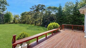 Eine Holzterrasse mit einer Bank, umgeben von einem gepflegten Rasen und Bäumen.
