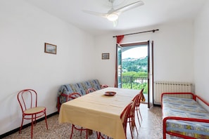 Une pièce comprenant un lit, une table, des chaises, un ventilateur de plafond et une fenêtre donnant sur un paysage verdoyant.