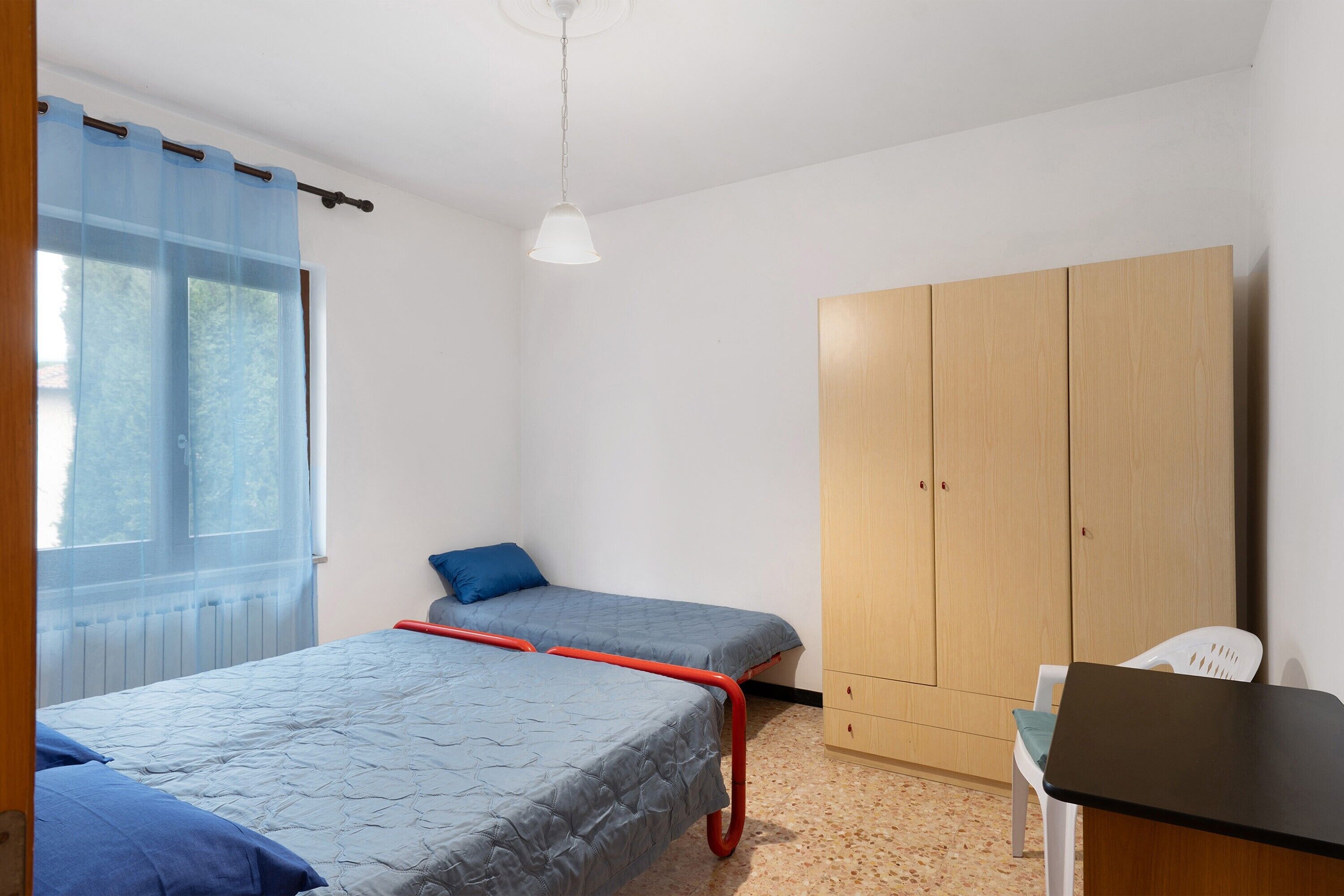 Une chambre avec deux lits, une armoire, une table et une fenêtre avec des rideaux.