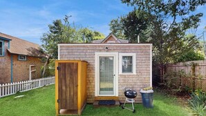A small brick house with a wooden door, a window, and a barbecue grill in the yard. - Cozy island cottage near local attractions with breezy yard & inviting interior (Oak Bluffs)