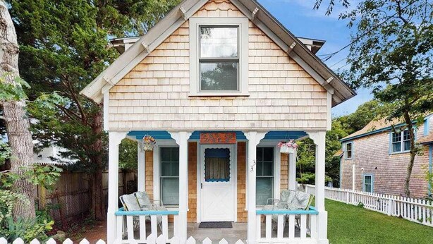 A two-story house with a porch, a front door, and a small sign above the door. - Cozy island cottage near local attractions with breezy yard & inviting interior (Oak Bluffs)