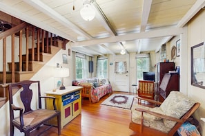 A spacious living area with a wooden staircase, a sofa, a chair, a small table, and a door leading to another room.