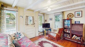 A cozy room with a bed, a desk, a television, and a bookshelf. - Cozy island cottage near local attractions with breezy yard & inviting interior (Oak Bluffs)