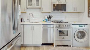 Een moderne keuken met witte kasten, roestvrijstalen apparatuur, een vaatwasser, een oven, een magnetron en een wasmachine.