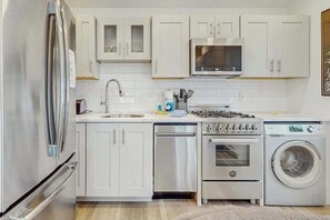 A modern kitchen with white cabinets, stainless steel appliances, a dishwasher, an oven, a microwave, and a washing machine. - Cozy Downtown Studio Near Beach and Commercial Street (Provincetown)