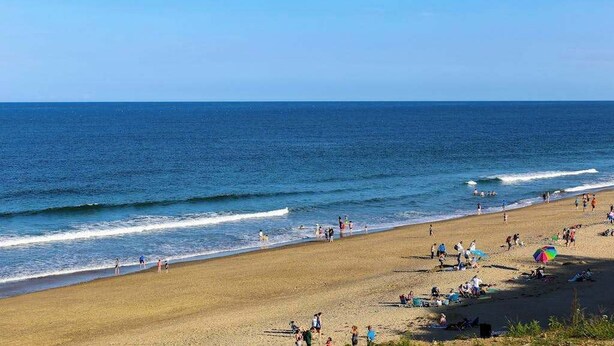 Een strand met mensen, een heldere lucht en de oceaan.