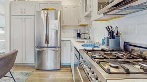 Een moderne keuken met roestvrijstalen apparatuur, witte kastjes, een gasfornuis en een eethoek met een stoel.