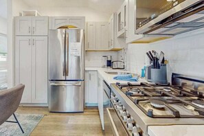 A modern kitchen with stainless steel appliances, white cabinetry, a gas stove, and a dining area with a chair. - Cozy Downtown Studio Near Beach and Commercial Street (Provincetown)
