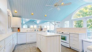 Una cocina con armarios blancos, una isla central, horno empotrado y ventilador de techo.