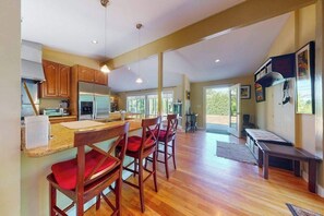 A spacious kitchen with wooden cabinets, a stainless steel refrigerator, and a bar area with red chairs. - Coastal home with outdoor shower, grill, fireplace, central AC, & W/D (Oak Bluffs)
