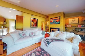 A living room with a white sofa set, a fireplace, and a bookshelf. - Coastal home with outdoor shower, grill, fireplace, central AC, & W/D (Oak Bluffs)