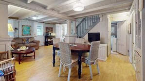 A spacious living room with a dining table, chairs, a sofa, and a staircase leading to another level. - Spacious colonial home close to town with AC, porches, & W/D (Oak Bluffs)
