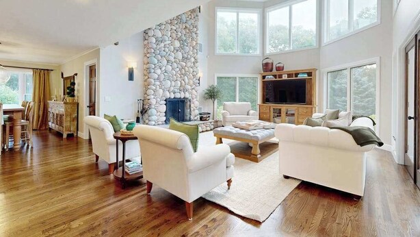 A spacious living room with a stone wall, a fireplace, a television, and large windows. - Enchanting home with tennis, firepit, golf nearby & washer/dryer (Oak Bluffs)