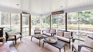 A covered patio with wicker furniture, a stone wall, and a sign reading 'OAK BLUFFS.' - Enchanting home with tennis, firepit, golf nearby & washer/dryer (Oak Bluffs)