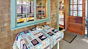 Quarto com porta de madeira, janela com vista e mesa com toalha de mesa estampada.