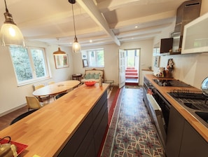 A modern kitchen with a wooden island, a dining area with a table and chairs, and a staircase leading to an upper level. - Le Clos Morlaisien (Morlaix)