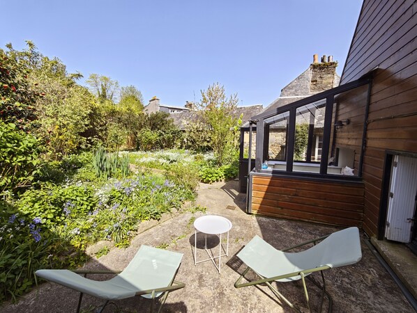 A garden with two chairs and a table, a wooden deck, and a stone wall. - Le Clos Morlaisien (Morlaix)