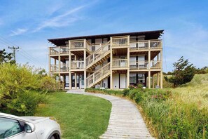 A multi-story building with balconies, a wooden deck, and a pathway leading to the entrance.