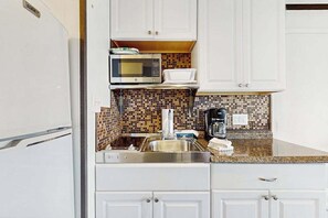 A kitchen with white cabinets, a microwave, a sink, and a tiled backsplash.