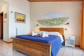 A bedroom with a wooden bed, a nightstand, a wall-mounted lamp, and a painting of a landscape. - Apartment 'Camera Familiare Classic' with Lake View, Shared Garden and Wi-Fi (Toscolano Maderno)