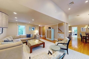 A spacious living room with a sofa, coffee table, and armchair, wooden flooring, and a staircase leading to another level. - Private pool close to beach with cabana, grill, AC, patio, dog-friendly (Mashpee)