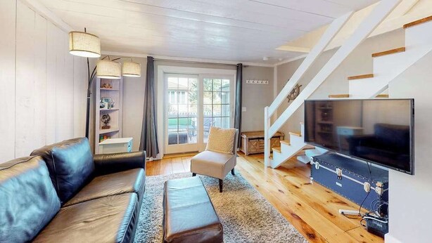 Una sala de estar moderna con un sofá de cuero, un sillón pequeño, un televisor de pantalla plana, una escalera y una estantería.