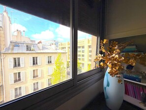 Ein Fenster mit Blick auf ein Gebäude mit mehreren Balkonen und einem Baum davor.