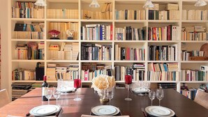 Un coin repas avec une table en bois foncé, dressée pour quatre personnes, entourée d’étagères blanches remplies de livres.