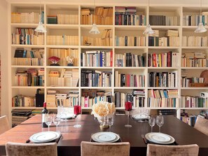 Ein Essbereich mit einem dunklen Holztisch, gedeckt für vier Personen, umgeben von weißen Bücherregalen voller Bücher.