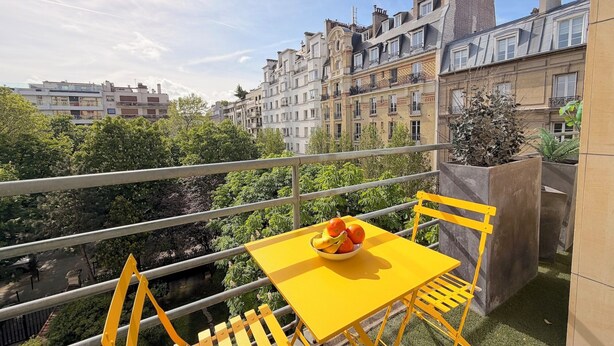 Une table et une chaise jaunes sur un balcon, avec vue sur des immeubles résidentiels et la verdure.