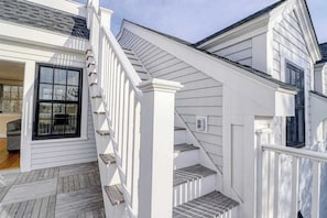A white exterior with a wooden deck, a staircase, and a window. - Historic, dog-friendly beach view house with fast WiFi, ocean view, & grill (Oak Bluffs)