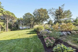 A well-maintained garden with a variety of plants and trees, a clear sky, and a house in the background. - Waterfront property with private dock and access to Nantucket Sound (West Dennis)
