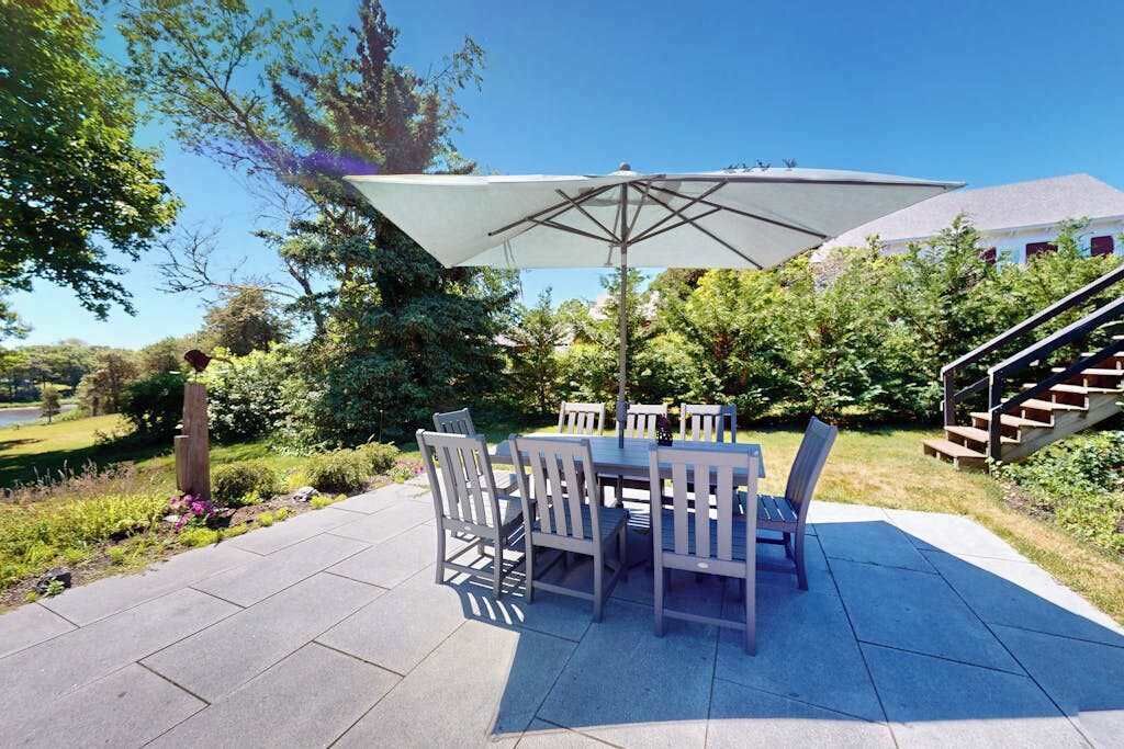 An outdoor patio with a table and chairs, a large umbrella, and a staircase leading to a building.