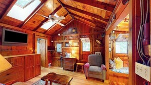 A cozy cabin interior with a wooden ceiling, a television, a sofa, a chair, and a small table. - Drummer Cove Gem | Cottage in Wellfleet with patio, steps from the cove (Wellfleet)
