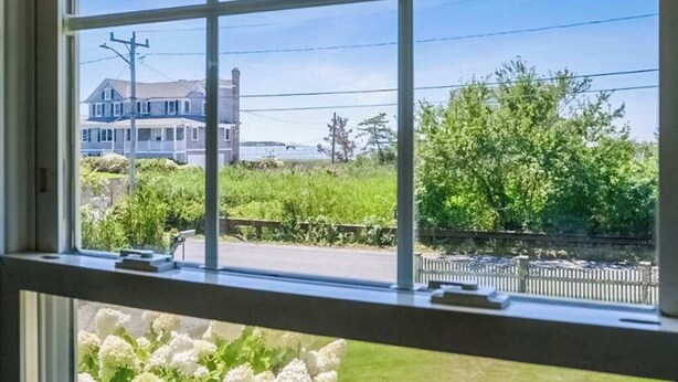 A window with a view of a house, greenery, and a fence. - Coastal bay view home with patio, W/D, AC, & amazing location (West Yarmouth)