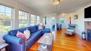 A spacious living room with a blue sectional sofa, a wooden coffee table, and a fireplace. - Coastal bay view home with patio, W/D, AC, & amazing location (West Yarmouth)
