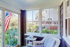 Ein Zimmer mit einem großen Fenster, einem Korbstuhl, einem kleinen Tisch und einer amerikanischen Flagge.
