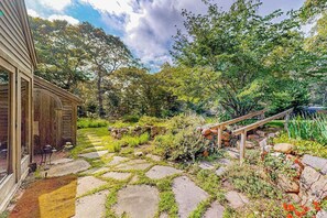 A garden with stone pathways, a wooden structure, and a wooden staircase. - Charming 2-story house near the beach with inviting deck, large yard & canoe (West Tisbury)