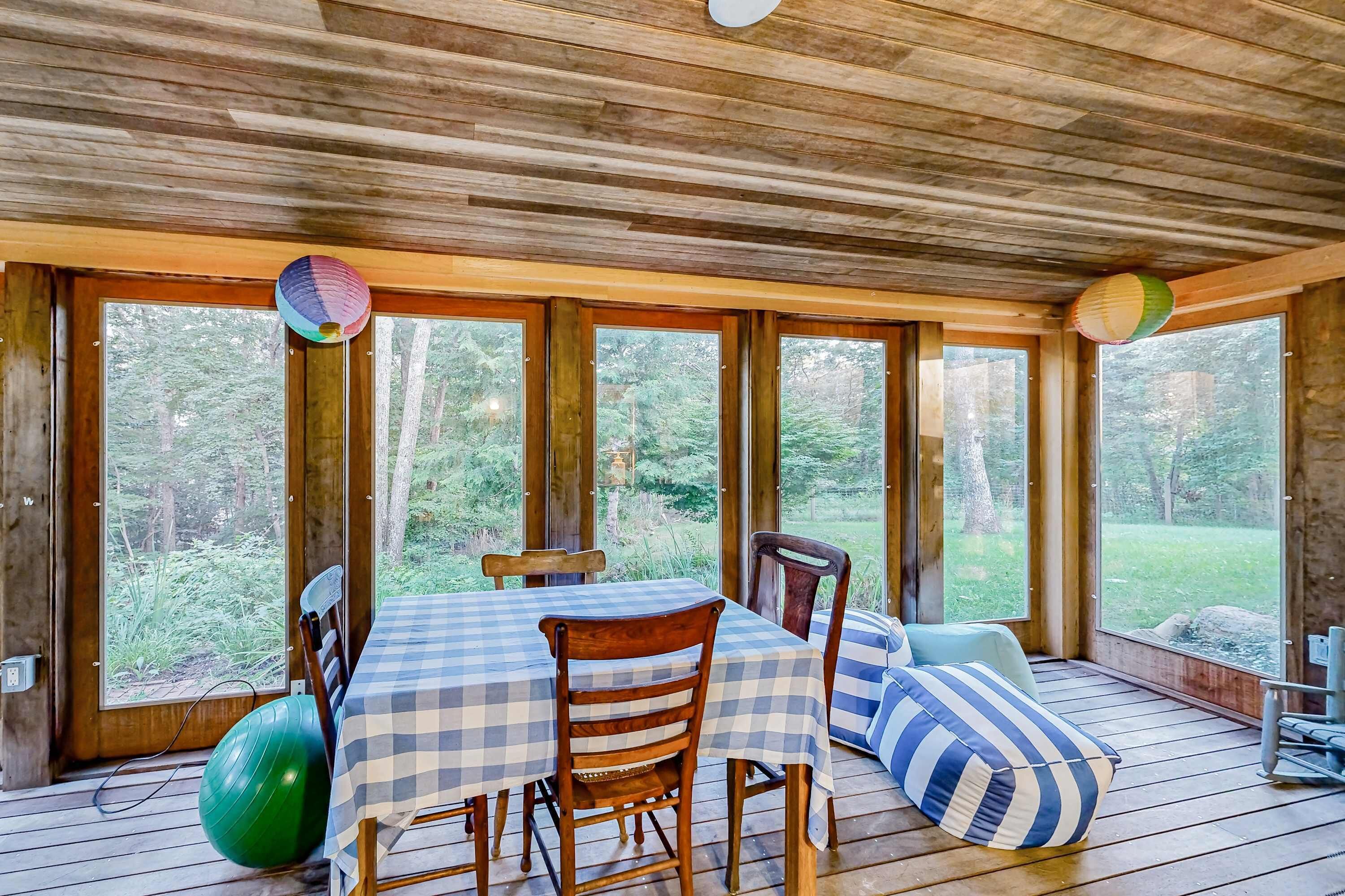 A wooden deck with a table and chairs, large windows, and a view of the outdoors.