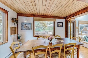 A wooden dining table with chairs, a window with a view, and a painting on the wall. - Charming 2-story house near the beach with inviting deck, large yard & canoe (West Tisbury)