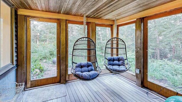 Techo de madera, dos sillones colgantes y amplias ventanas con vistas al bosque.